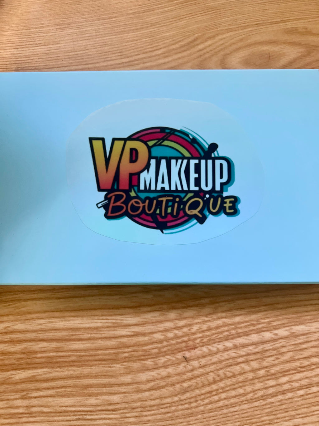 Vickipboutique ocean inspired makeup palette in sleek white packaging with colorful logo on wooden surface